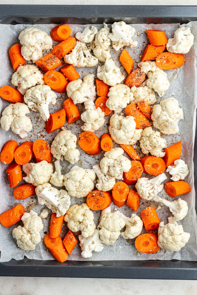 The veggies with oil and spices on a sheet pan.