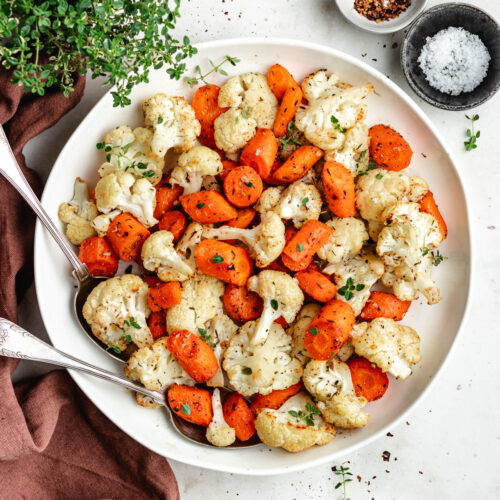 The roasted vegetables on a serving platter topped with fresh thyme.