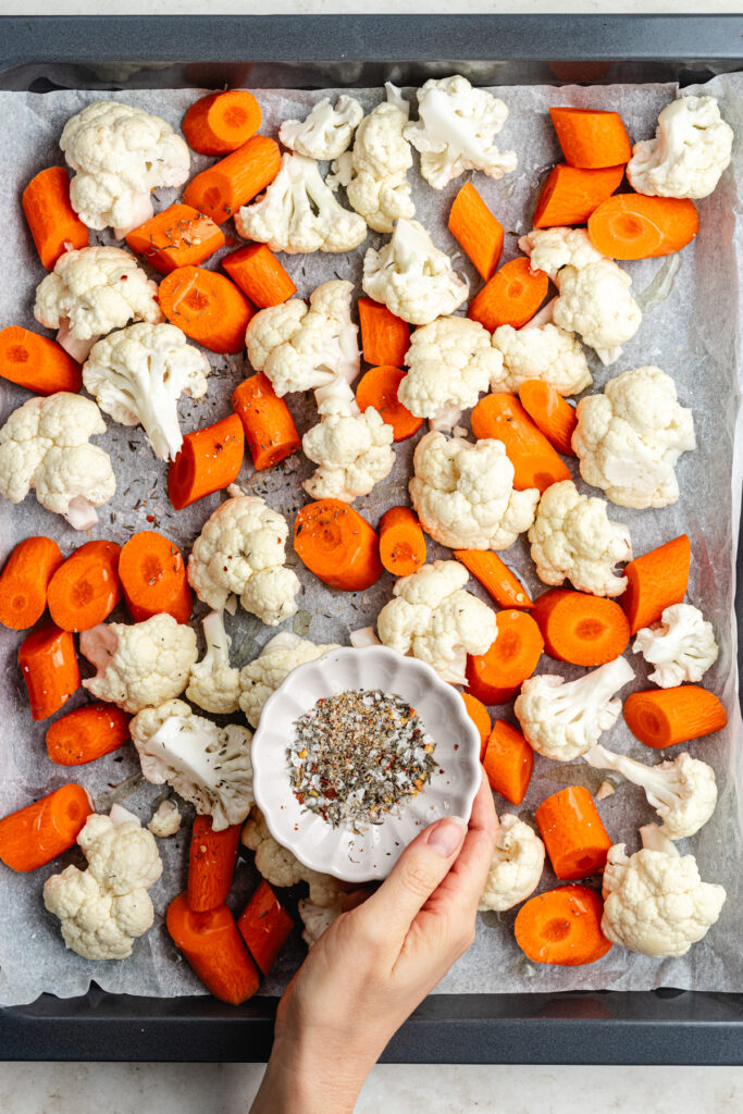 The vegetables on a sheet pan topped with oil and spices.