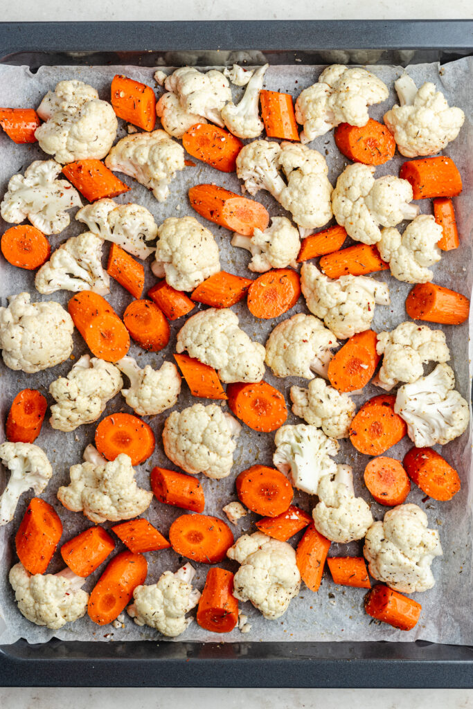 The vegetables tossed with oil and spices on a sheet pan.