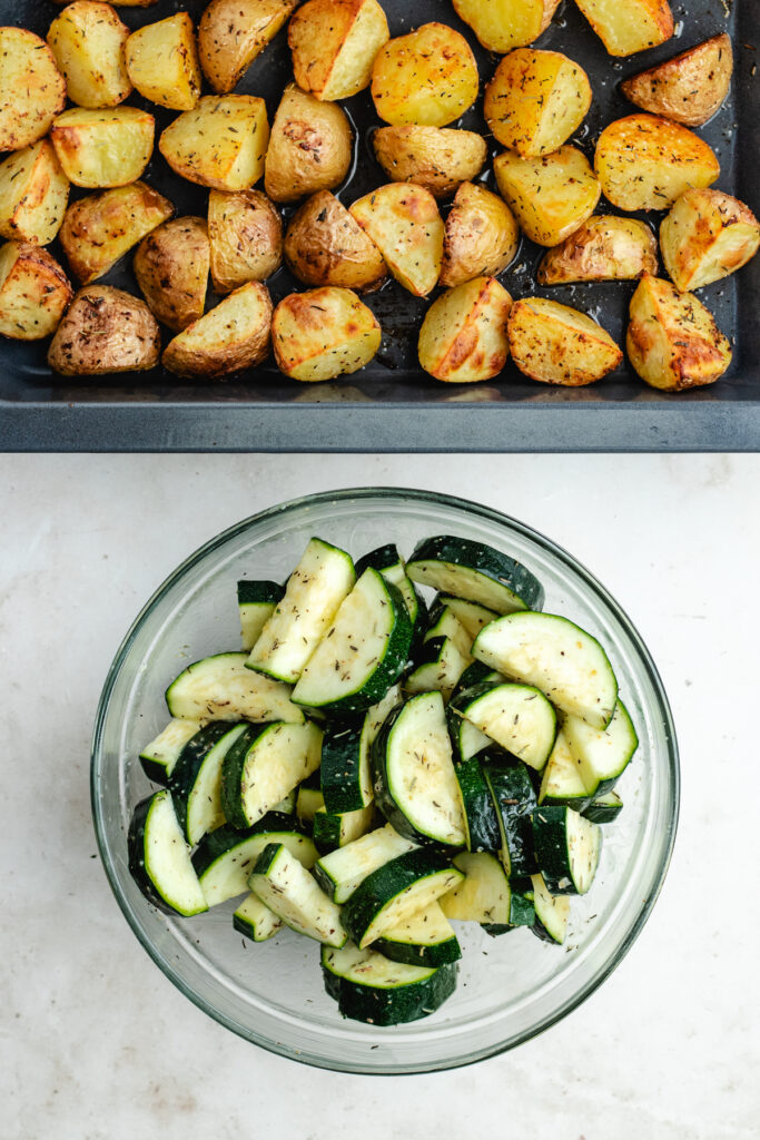 The zucchini in a bowl with the potatoes on the sheet pan.