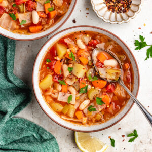 A bowl of soup with a spoon topped with fresh herbs.