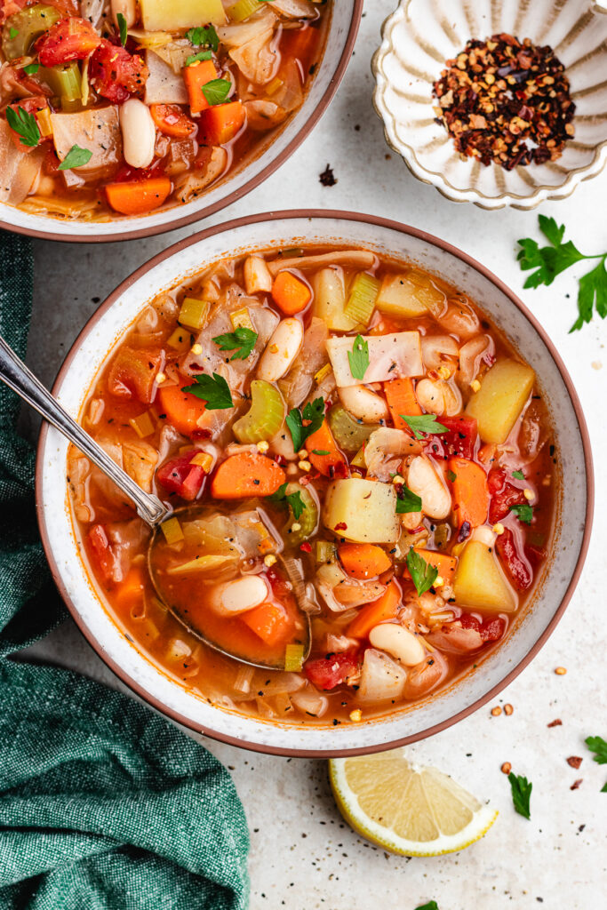 A bowl of soup with a spoon topped with fresh herbs.