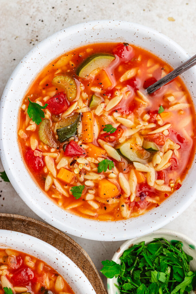 The soup in two bowls topped with red pepper flakes and chopped herbs.