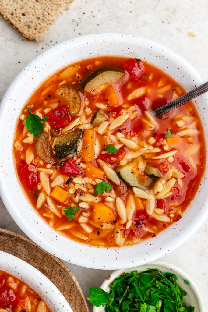 The soup in two bowls topped with red pepper flakes and chopped herbs.