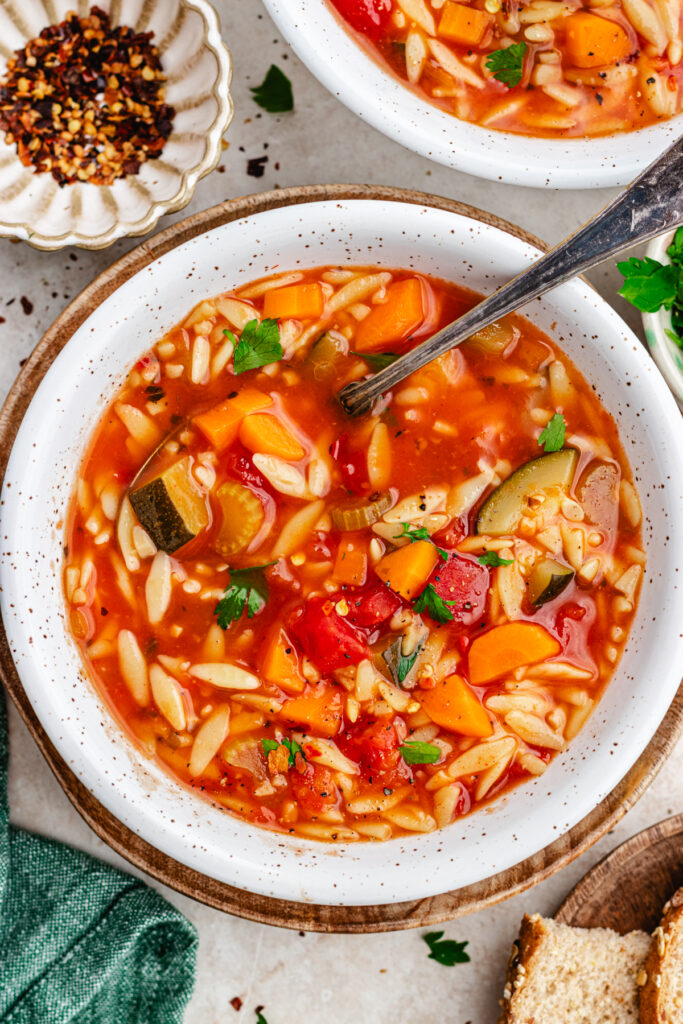 The soup in two bowls topped with red pepper flakes and chopped herbs.