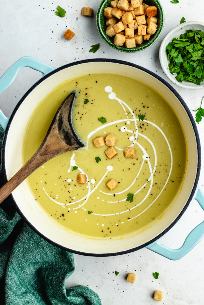 The cooked soup in the pot topped with drizzle of cream, croutons and fresh parsley.