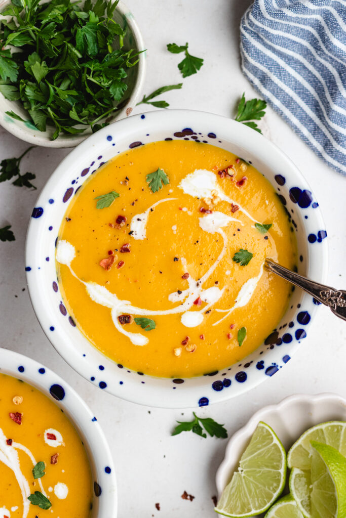 The soup in two bowls topped with some coconut milk, herbs and red pepper flakes.