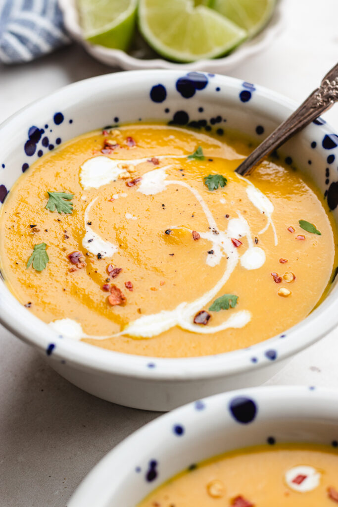 The soup in two bowls topped with some coconut milk, herbs and red pepper flakes.