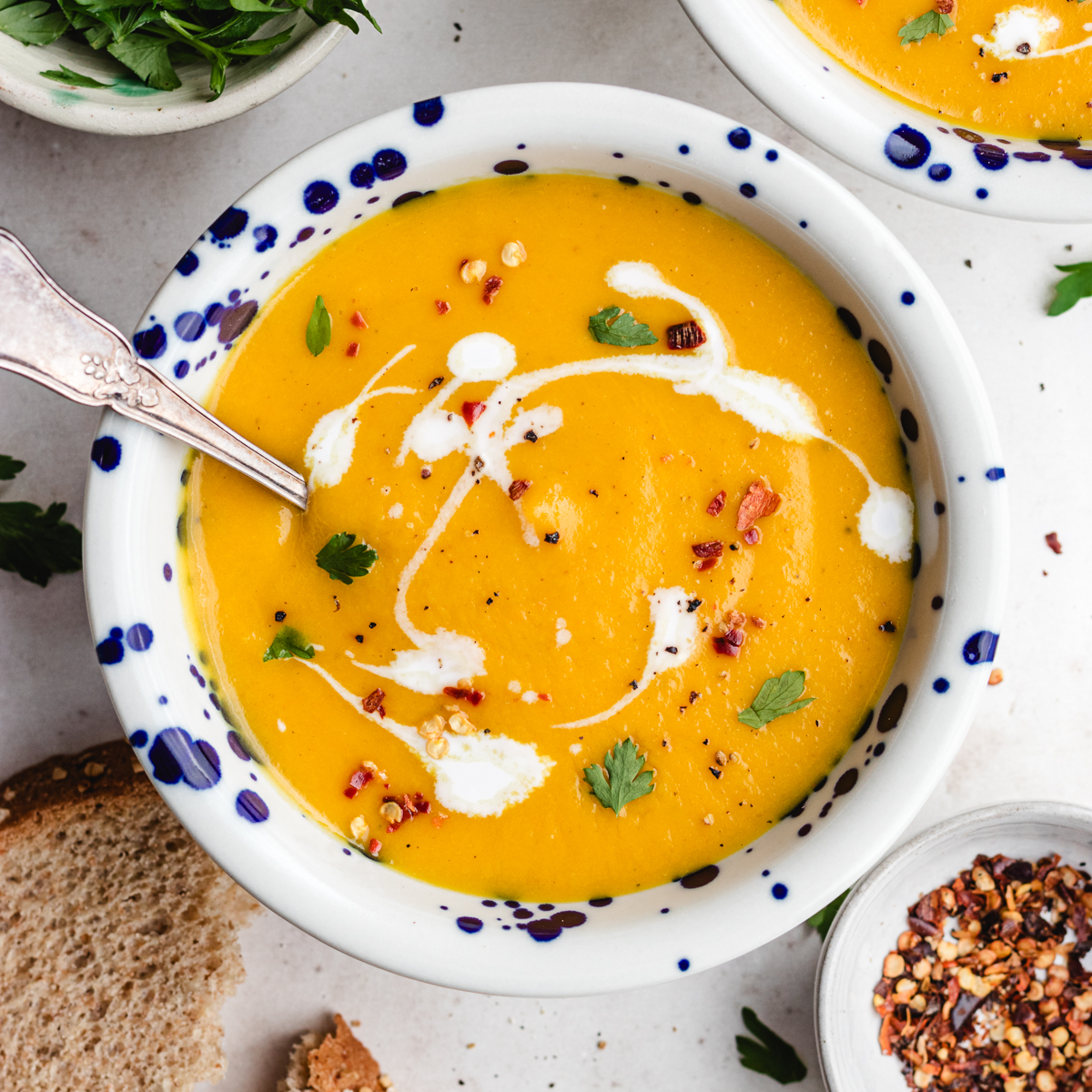 The soup in two bowls topped with some coconut milk, herbs and red pepper flakes.