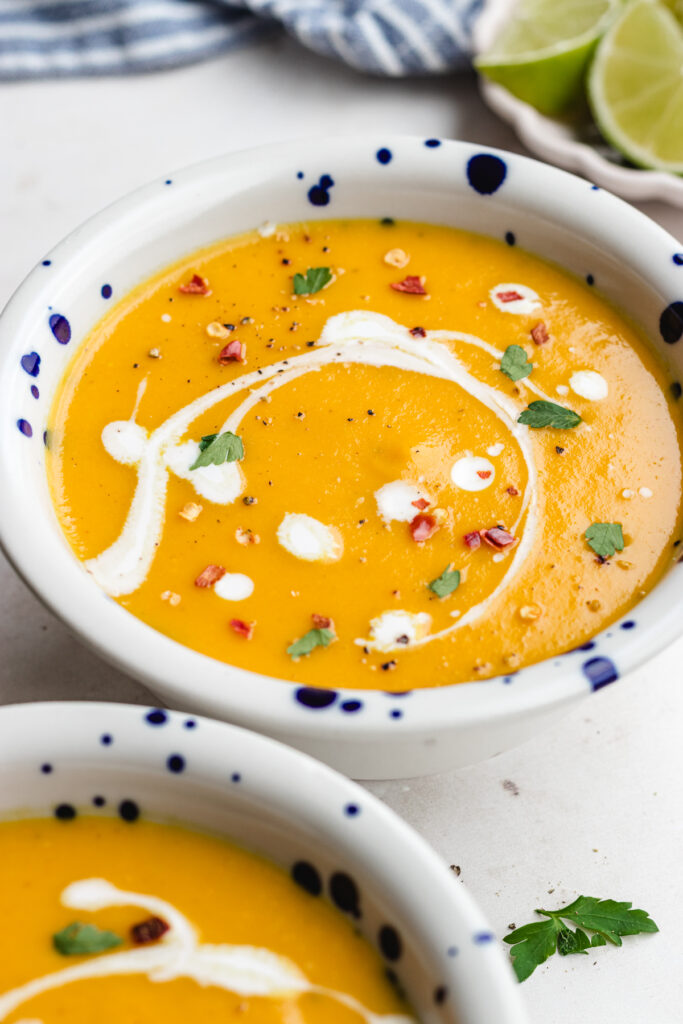 The soup in two bowls topped with some coconut milk, herbs and red pepper flakes.