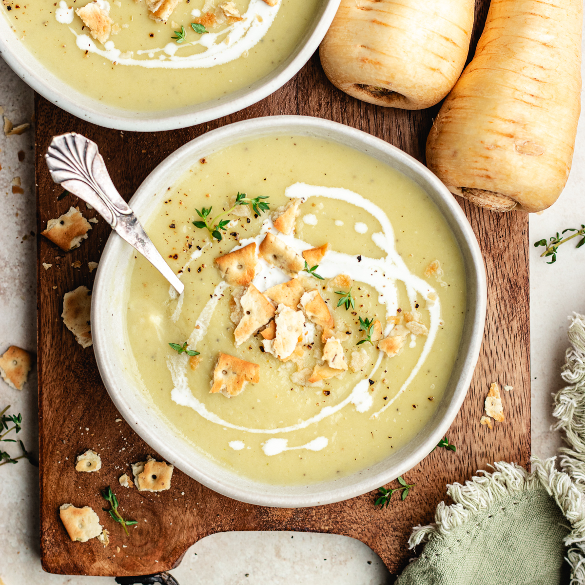 The soup in two bowls topped with cream, crackers and herbs.