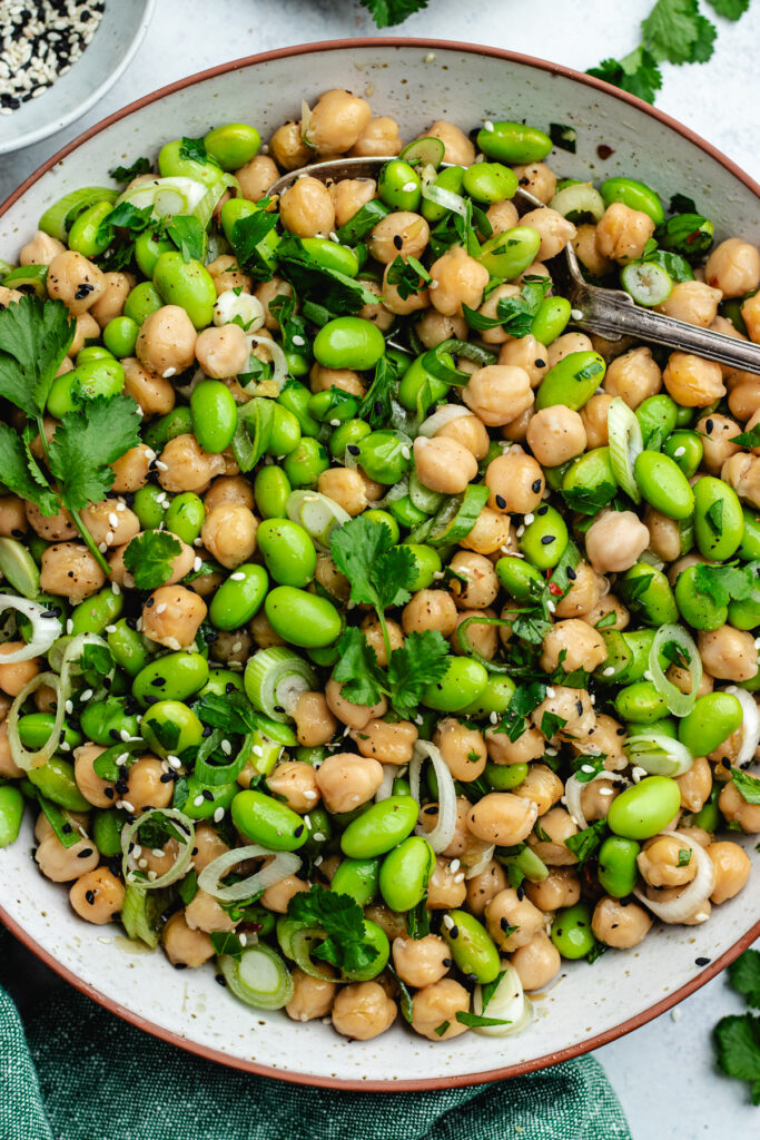The edamame and chickpeas salad in a bowl, topped with fresh herbs and sesame seeds.