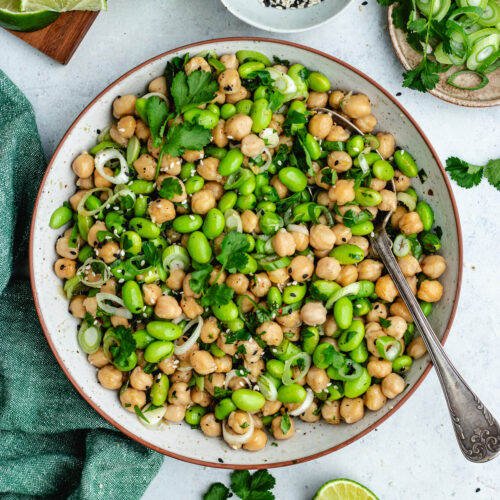 The edamame and chickpea salad in a bowl topped with fresh herbs and sesame seeds.