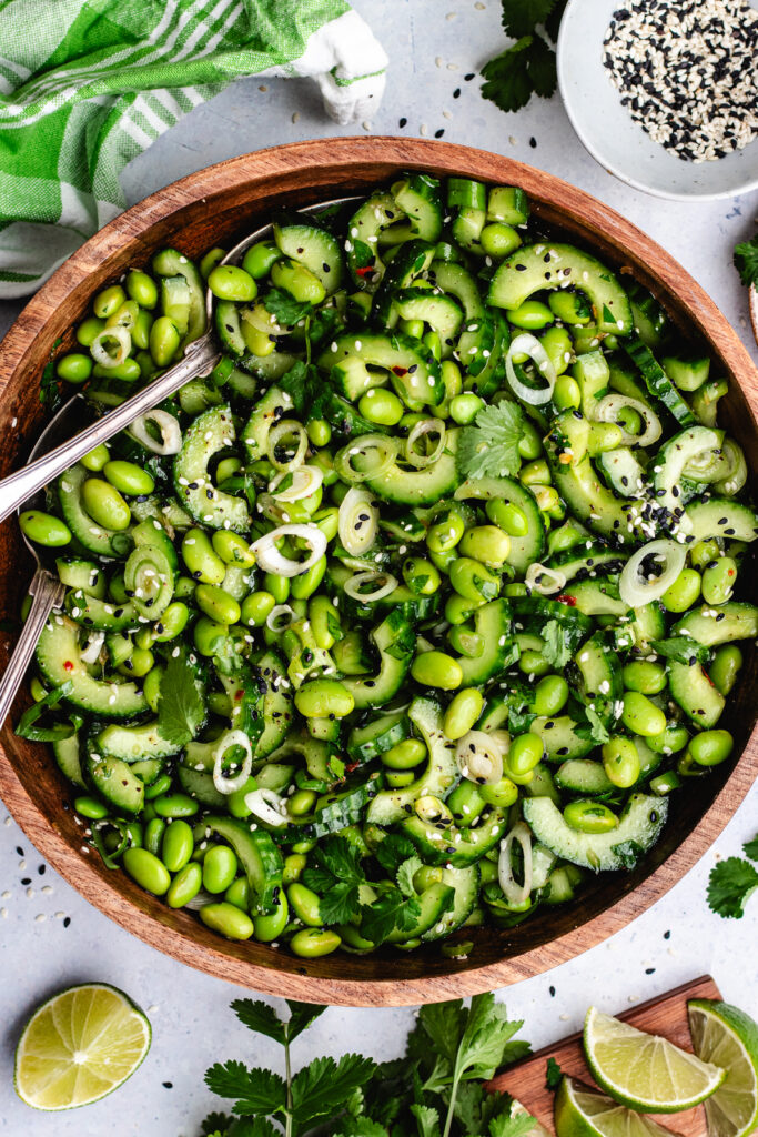 The edamame and cucumber salad in a wooden bowl topped with sesame seeds and fresh herbs. 