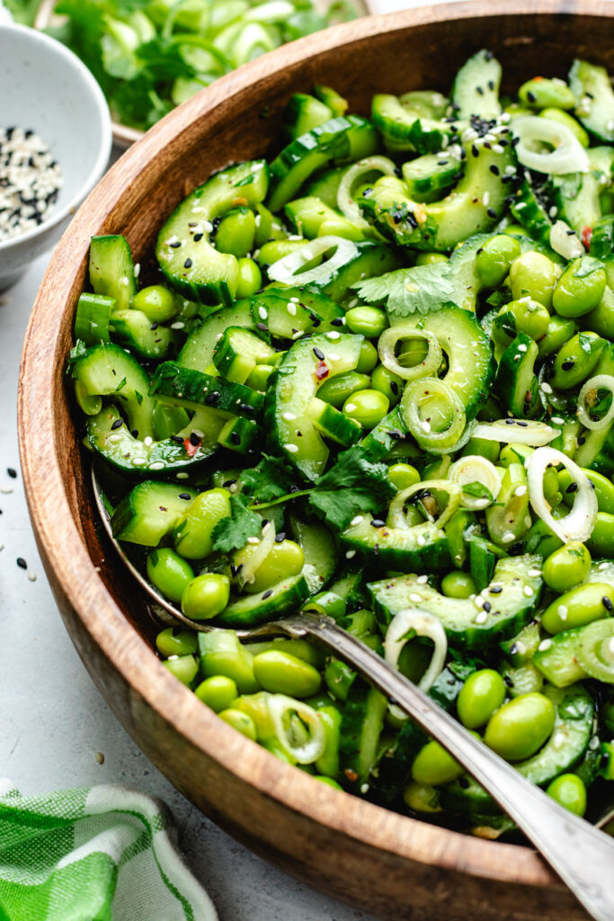 The edamame and cucumber salad in a wooden bowl topped with sesame seeds and fresh herbs.