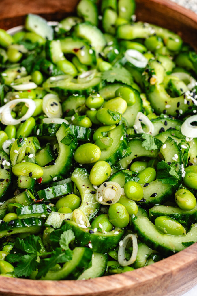The edamame and cucumber salad in a wooden bowl topped with sesame seeds and fresh herbs.