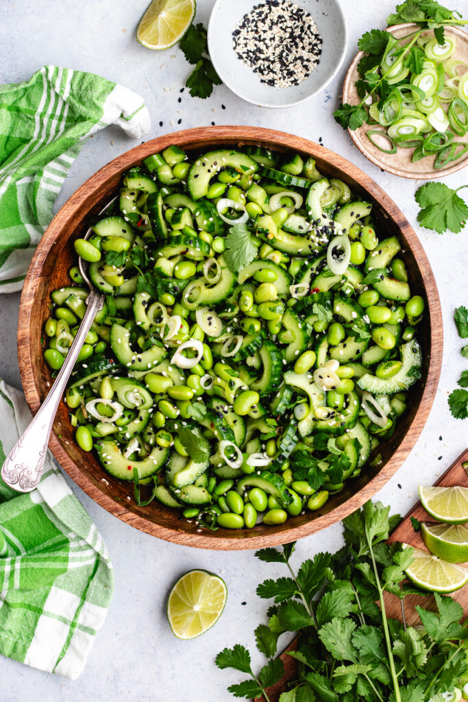 The edamame and cucumber salad in a wooden bowl topped with sesame seeds and fresh herbs.