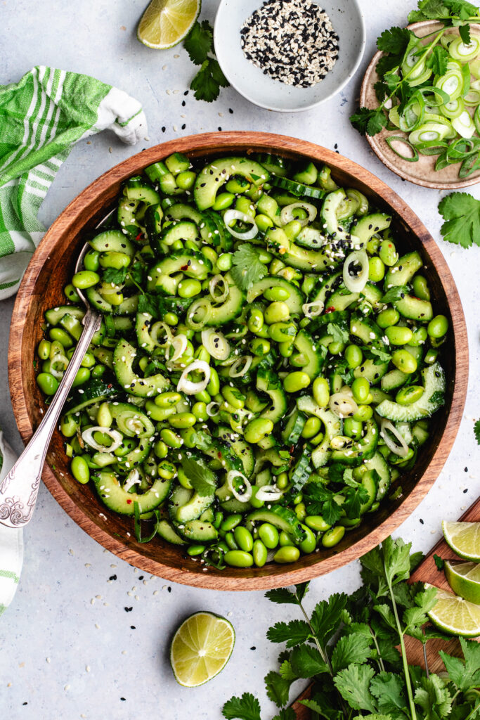 The edamame and cucumber salad in a wooden bowl topped with sesame seeds and fresh herbs.