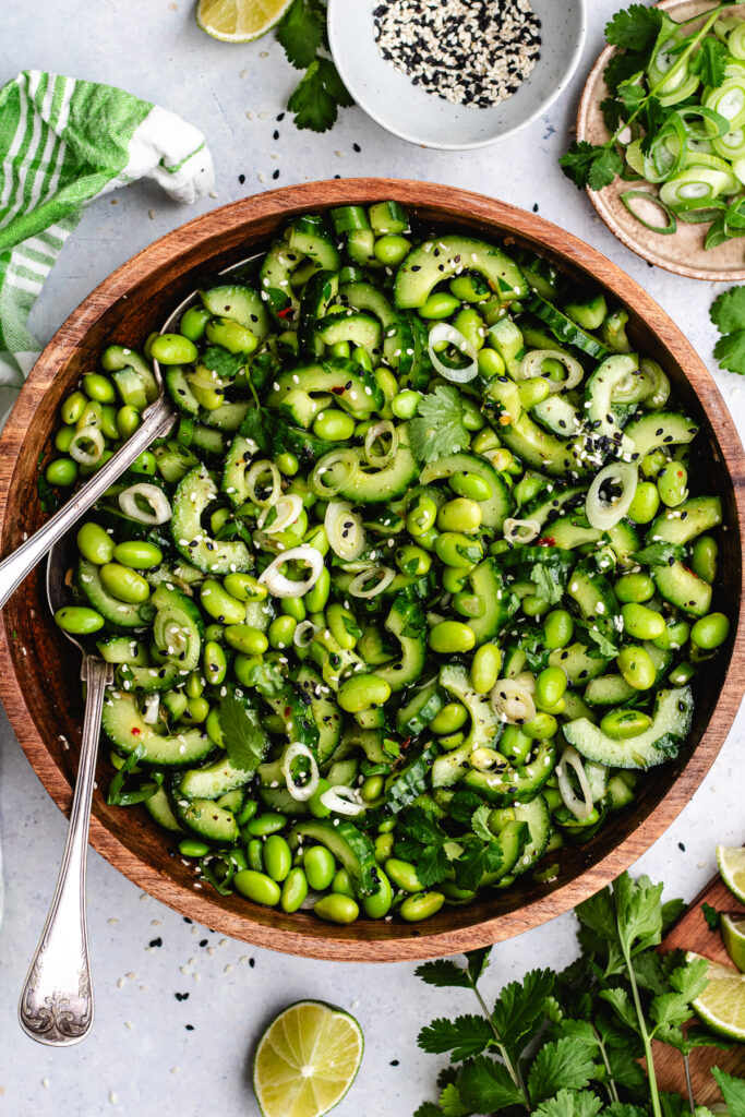 The edamame and cucumber salad in a wooden bowl topped with sesame seeds and fresh herbs.