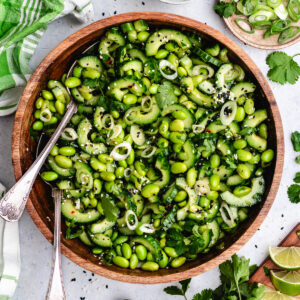 The edamame and cucumber salad in a wooden bowl topped with sesame seeds and fresh herbs.