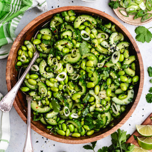 The edamame and cucumber salad in a wooden bowl topped with sesame seeds and fresh herbs.
