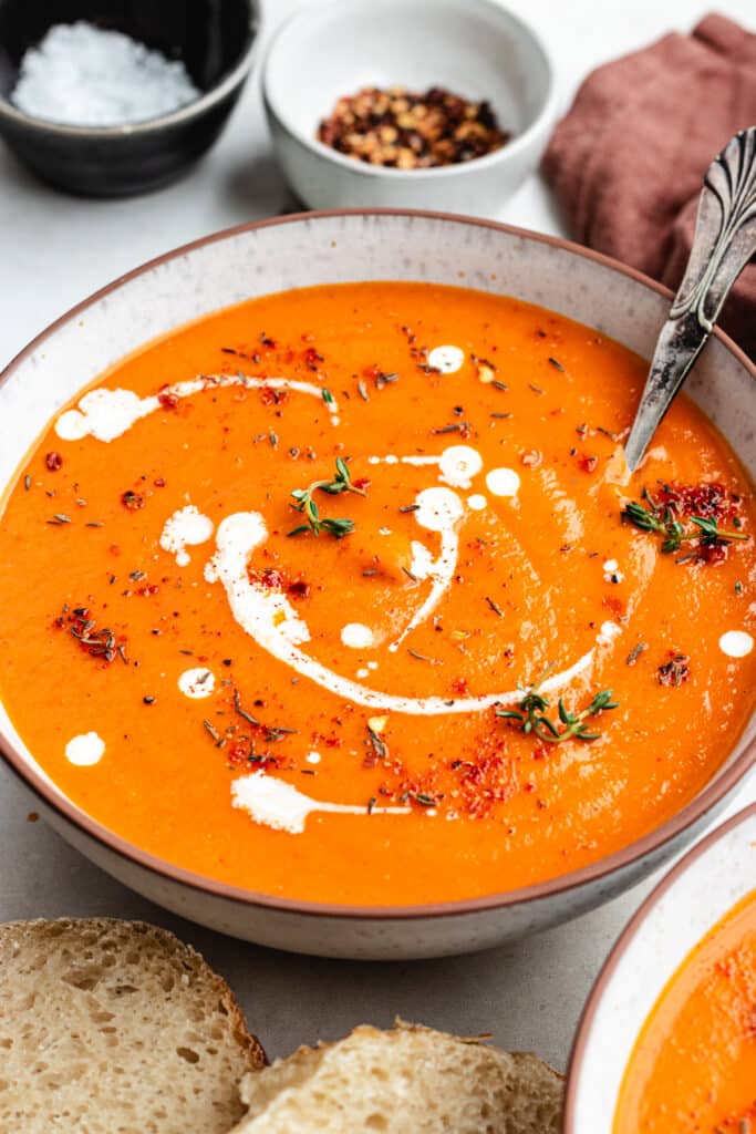 The roasted tomato and sweet potato soup in two bowls topped with a drizzle of cream, herbs and spices.