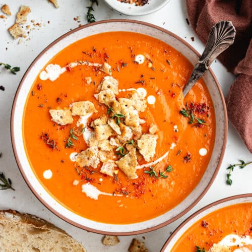 The soup in a bowl topped with crackers and herbs.