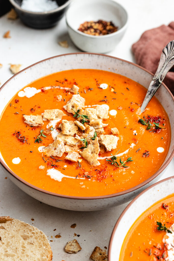 The soup in a bowl topped with crackers and herbs.