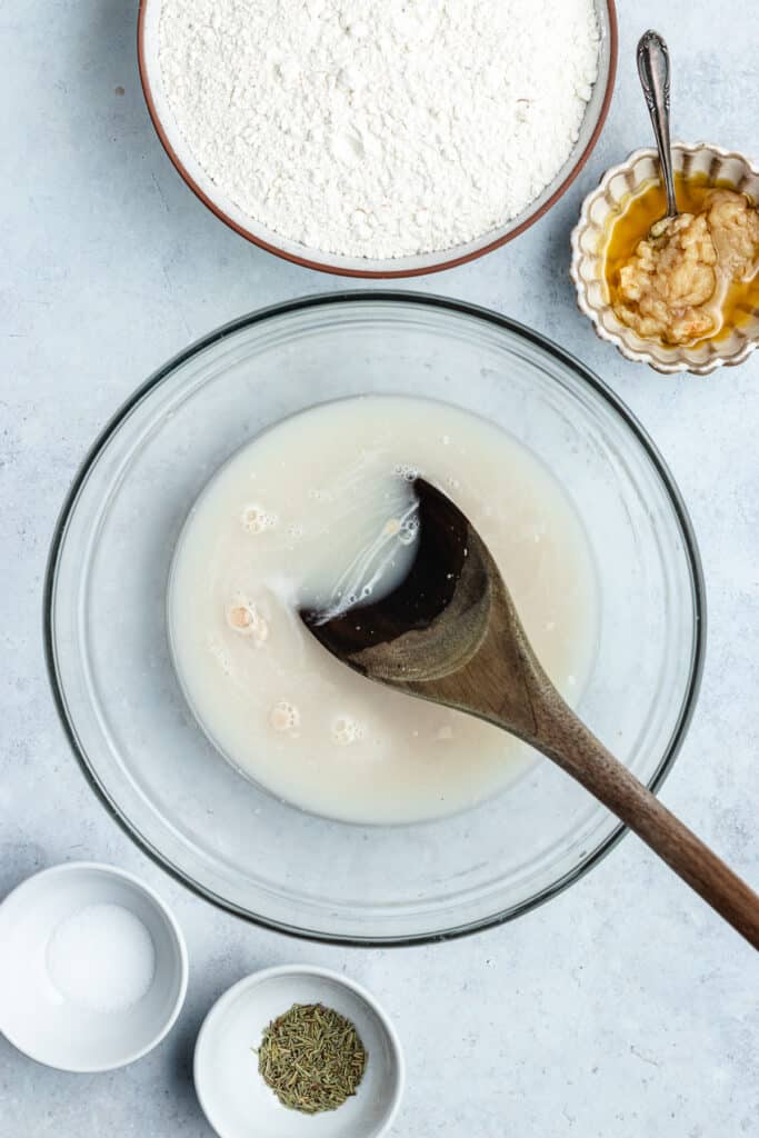 The water, yeast and sugar in a large bowl with a spoon.