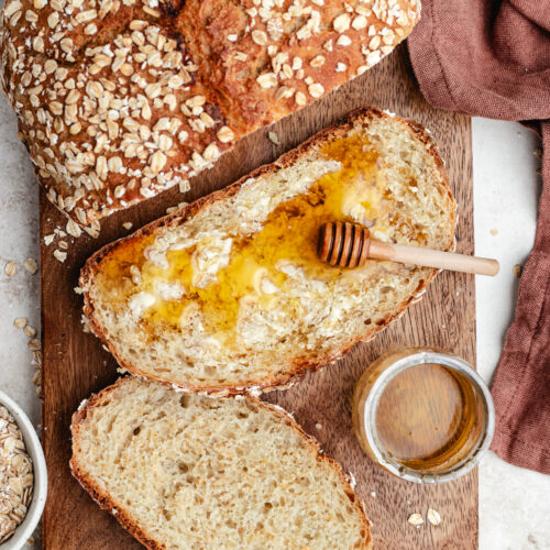 The oatmeal bread cut in slices topped with butter and honey.