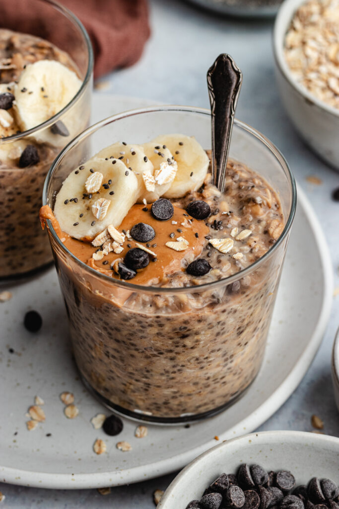 The overnight oats in 2 glasses topped with banana slices, peanut butter and chocolate chips.