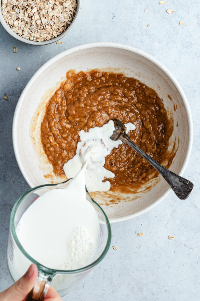 Pouring in the milk to the bowl with the mashed banana, peanut butter and maple syrup.