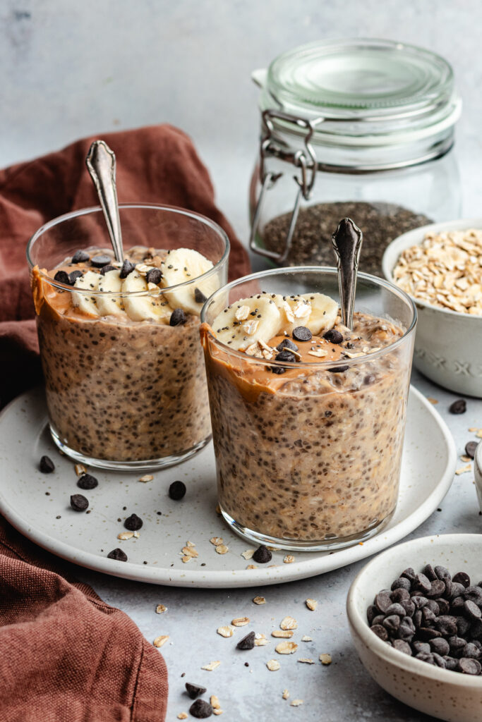The overnight oats in 2 glasses topped with banana slices, peanut butter and chocolate chips.