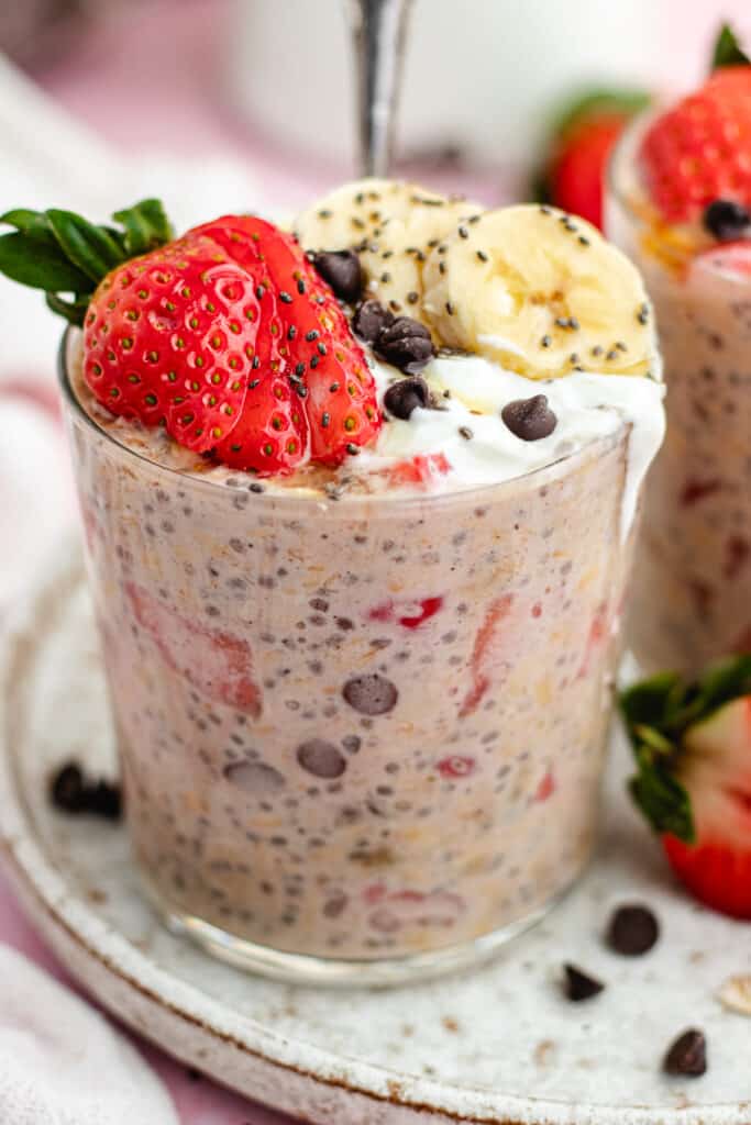 The overnight oats in a glass topped with yoghurt, strawberries, banana slices and chocolate chips.