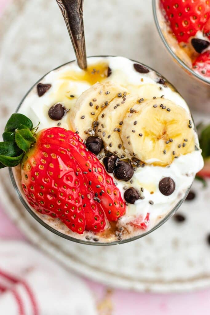 The overnight oats in a glass topped with yoghurt, strawberries, banana slices and chocolate chips.