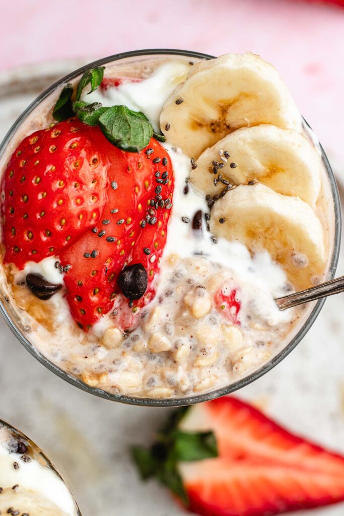 The overnight oats in a glass topped with yoghurt, strawberries, banana slices and chocolate chips.