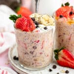 The overnight oats in a glass topped with yoghurt, strawberries, banana slices and chocolate chips.