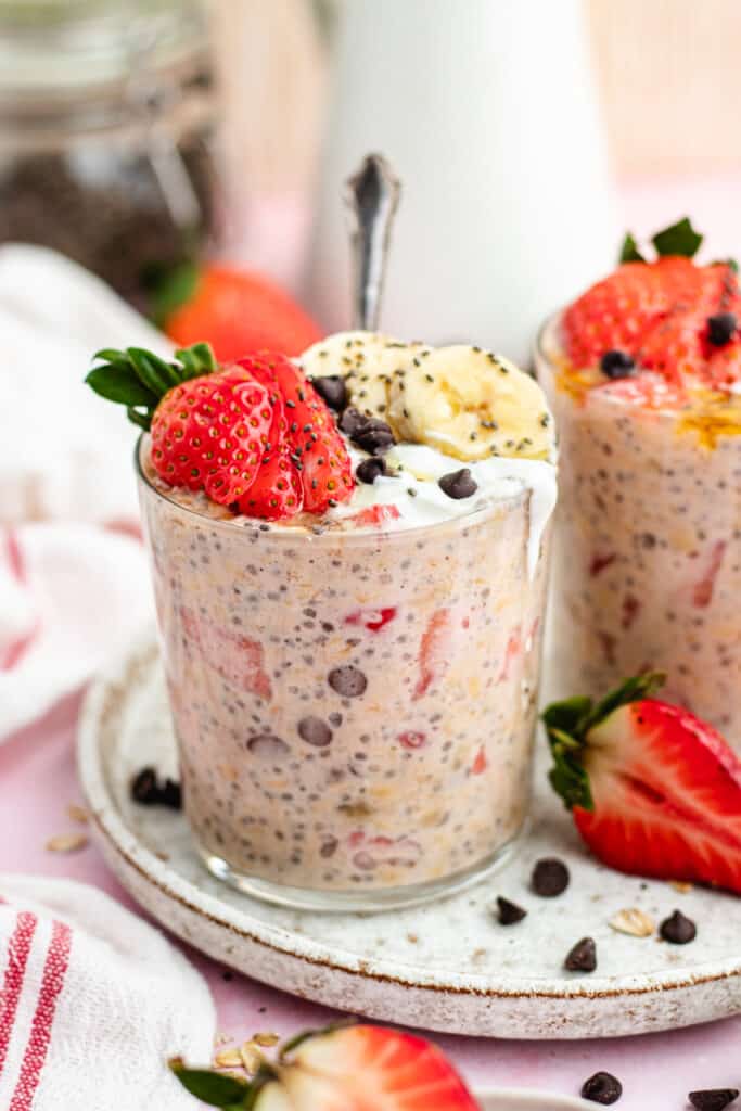 The overnight oats in a glass topped with yoghurt, strawberries, banana slices and chocolate chips. 
