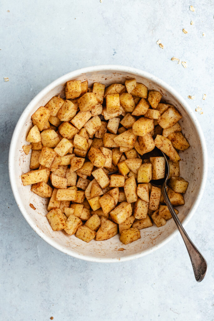 The apples with the cinnamon and maple syrup in a mixing bowl.
