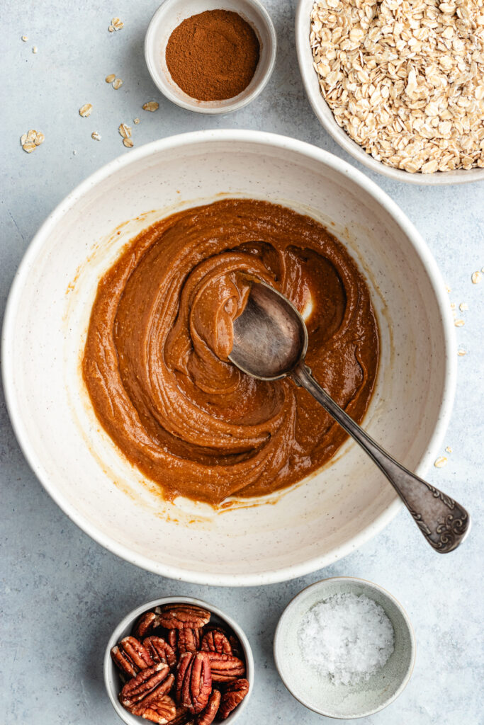 The nut butter and maple syrup stirred together with a spoon in a mixing bowl.