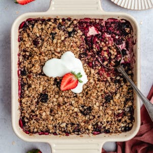The berry crumble in the baking dish topped with yoghurt.