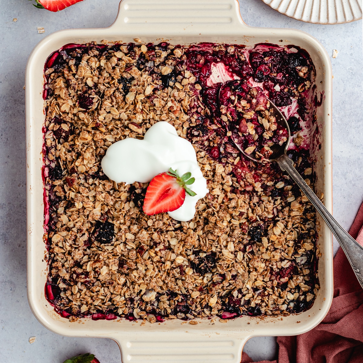 The berry crumble in the baking dish topped with yoghurt.