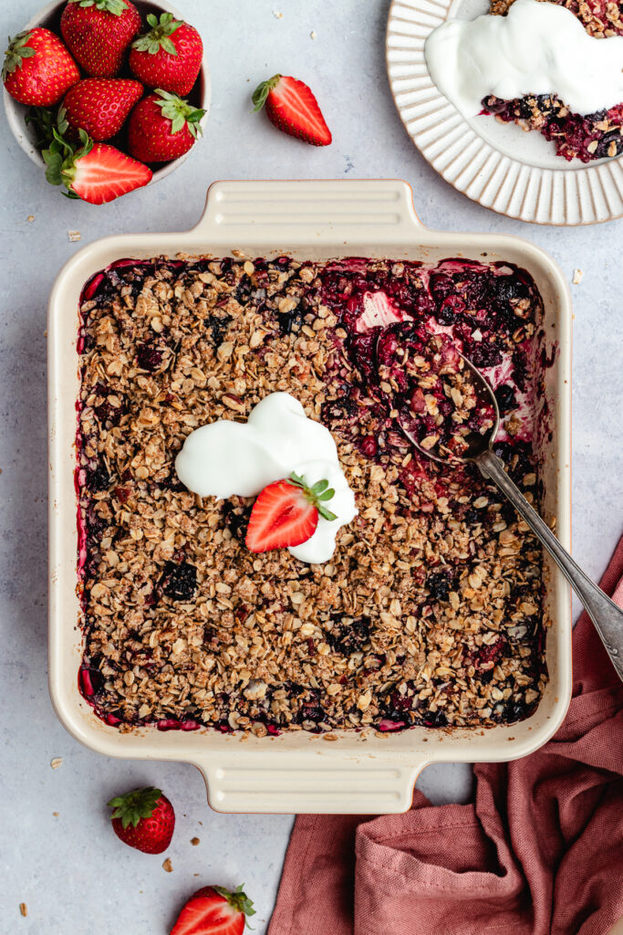 The berry crumble in the baking tray topped with yoghurt. 