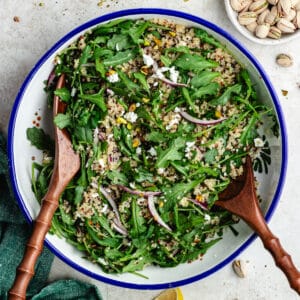 The salad in a salad bowl with lemon and pistachios on the side.
