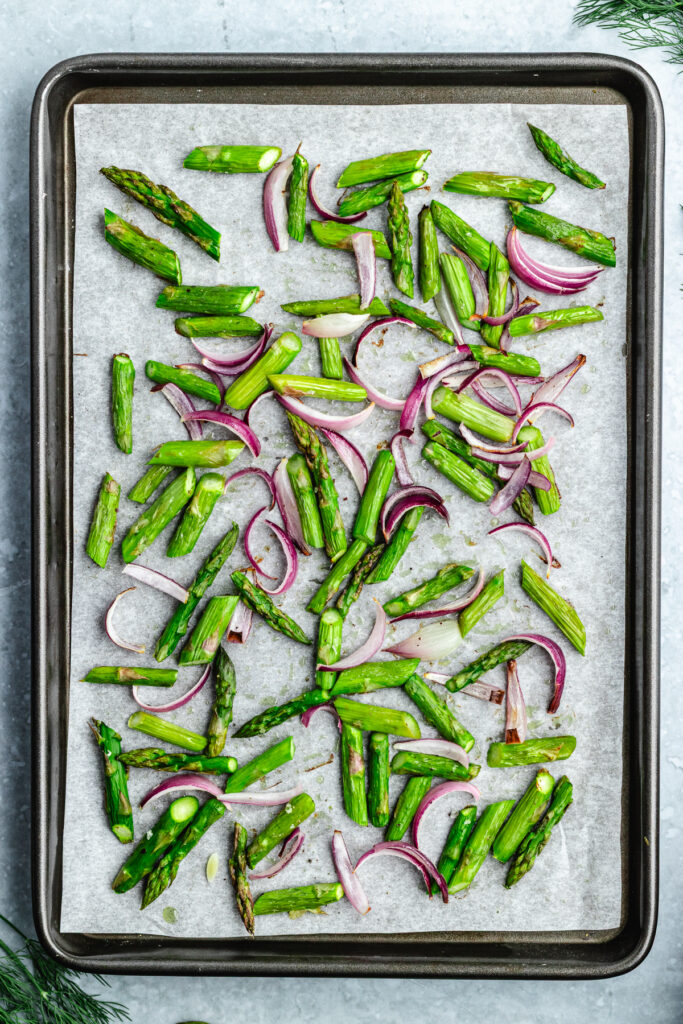 The roasted asparagus and red onion on a baking sheet.