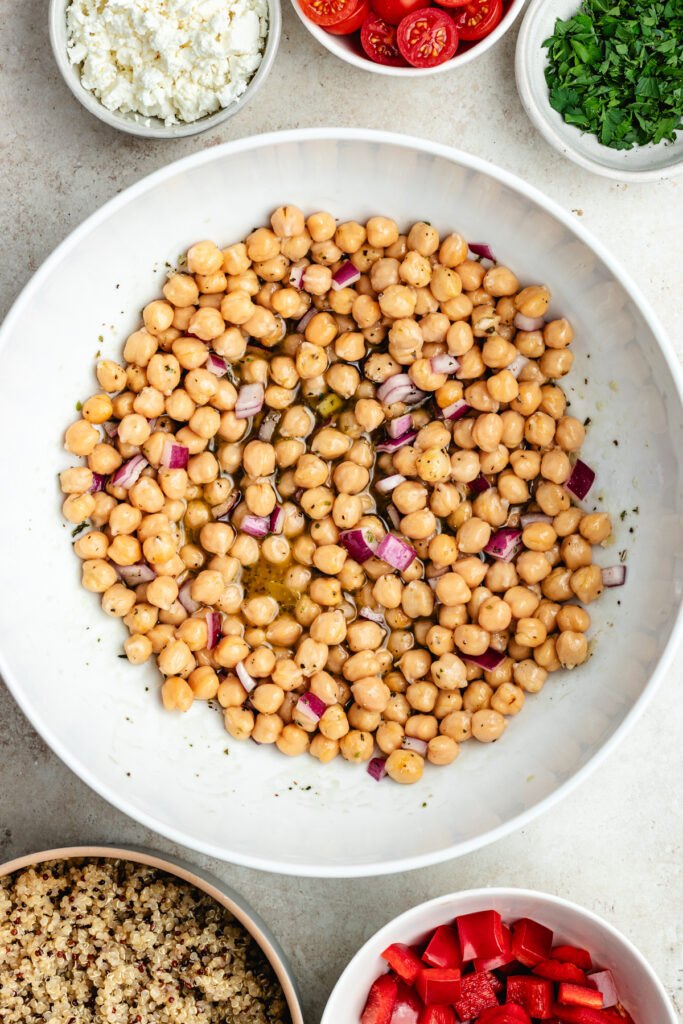 The chickpeas and chopped red onion in the salad bowl with the dressing.