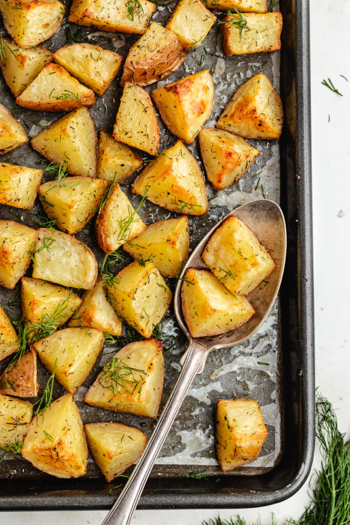 The roasted potatoes with a serving spoon on the baking tray.