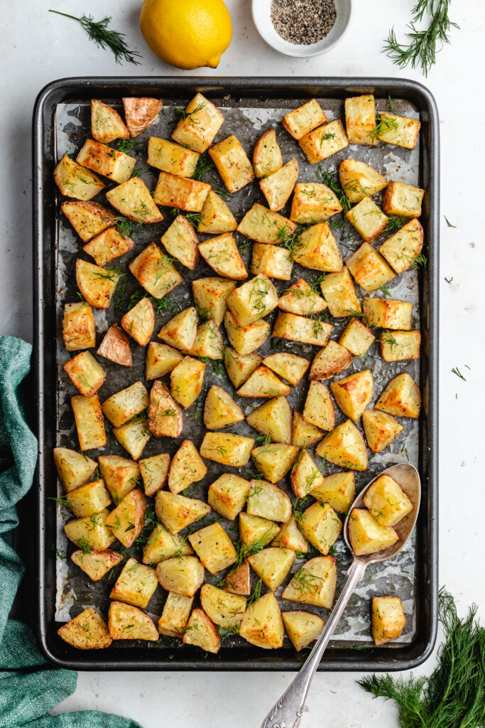 The roasted potatoes with a serving spoon on the baking tray.
