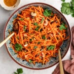 The carrot salad in a serving bowl topped with fresh herbs and chopped cashews.